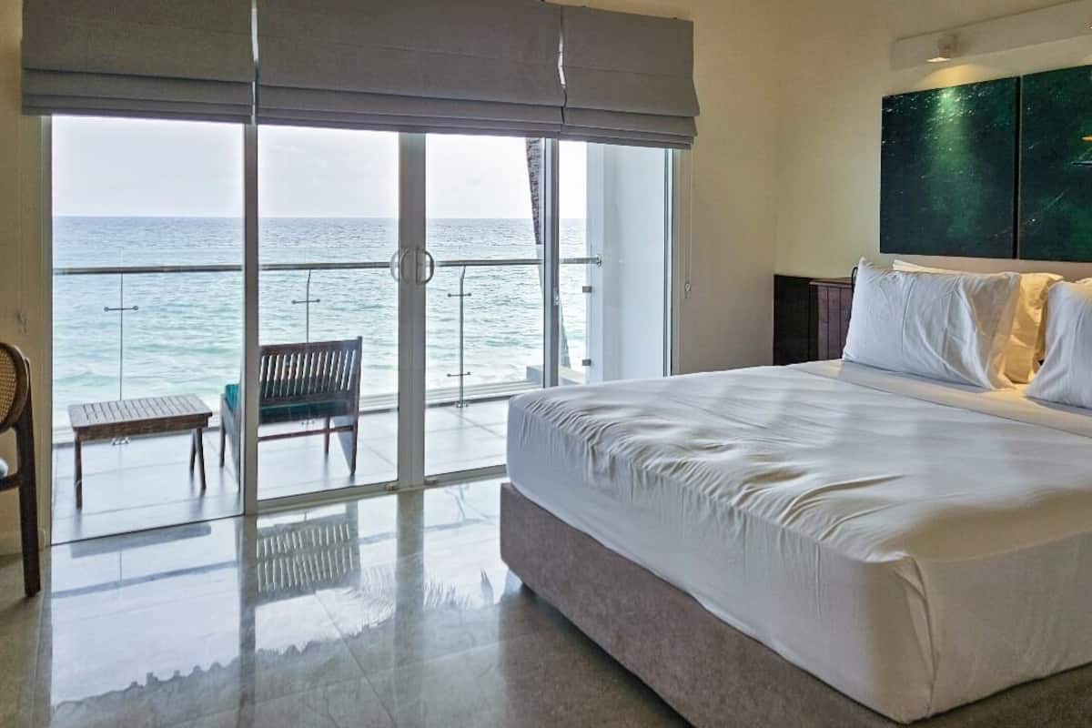 A bedroom with a large bed, a view of the sea through a sliding door, and a bench by the door.