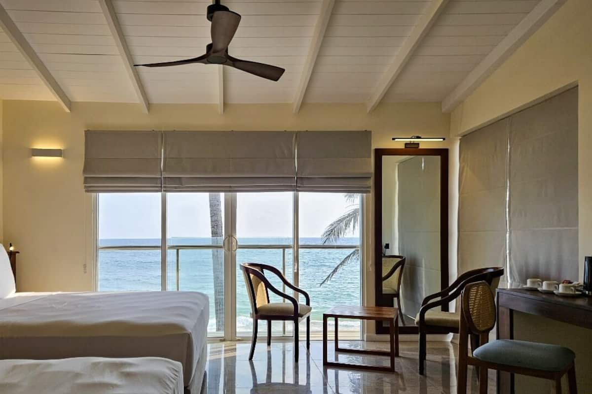 A hotel room with a bed, chairs, a desk, and a view of the ocean.
