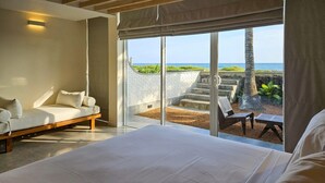 Une chambre avec un grand lit, un canapé et une vue sur l’océan, accessible par une porte-fenêtre coulissante.