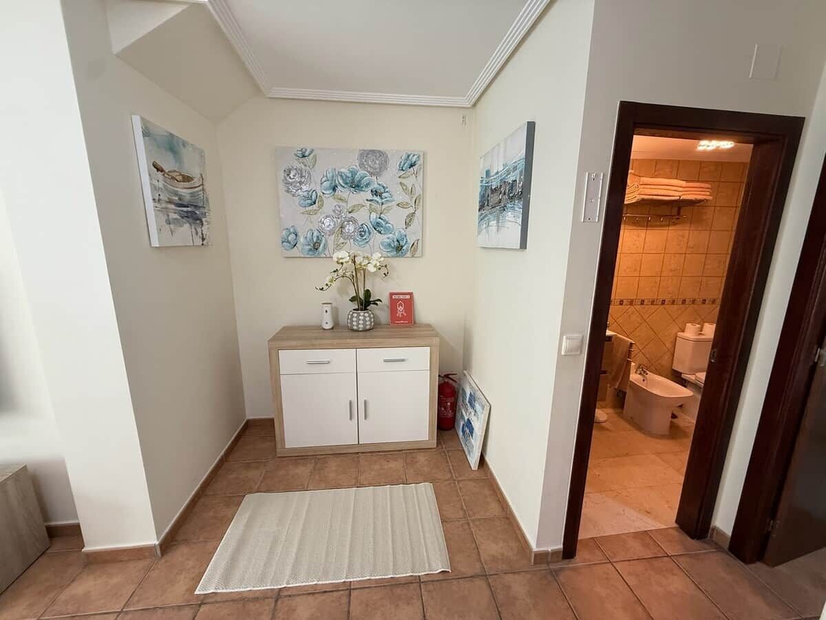 A hallway with a white cabinet, a rug, and artwork on the walls.