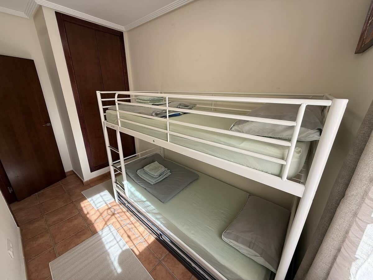 Uma cama beliche num quarto com porta e janela.