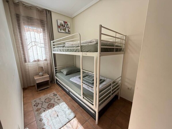A bunk bed room with a small bedside table, a window with curtains, and a rug on the floor.