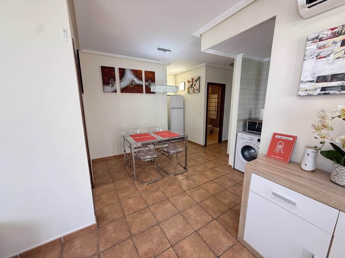 A compact kitchen with a dining table, a washing machine, and a refrigerator.