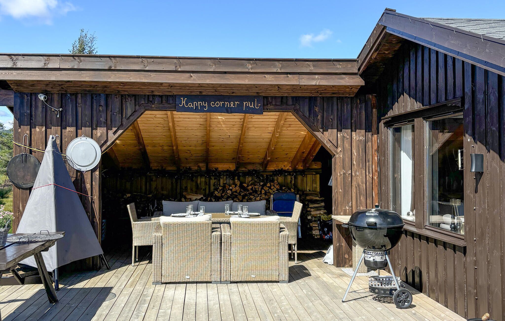 Un espace extérieur aménagé avec des meubles en bois, comprenant une table et des chaises, un barbecue et un panneau indiquant : « Règles du coin convivial ».