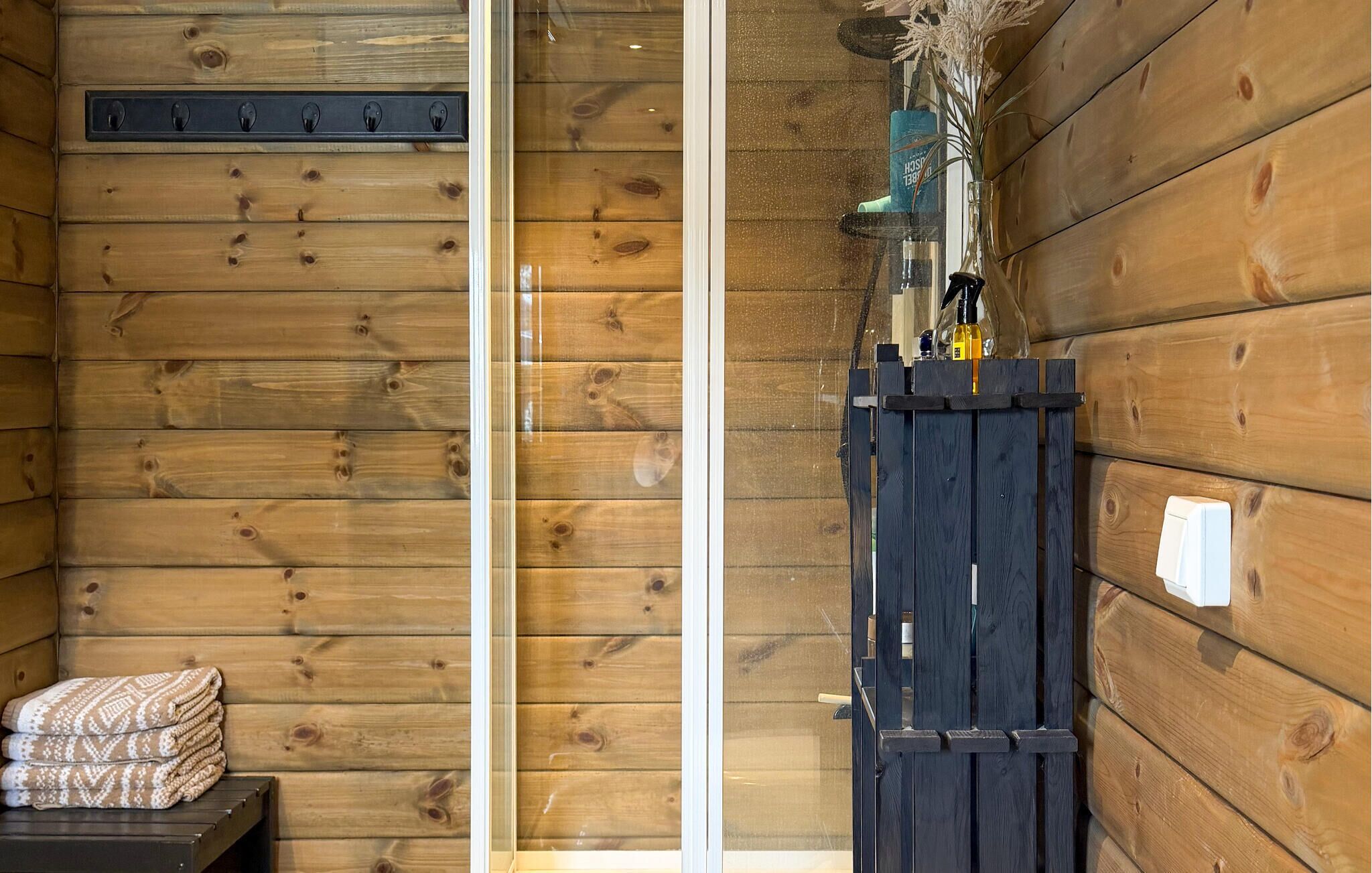 L’intérieur d’un chalet en bois, avec une porte en verre, un banc en bois recouvert de couvertures et un portail noir avec un vaporisateur.