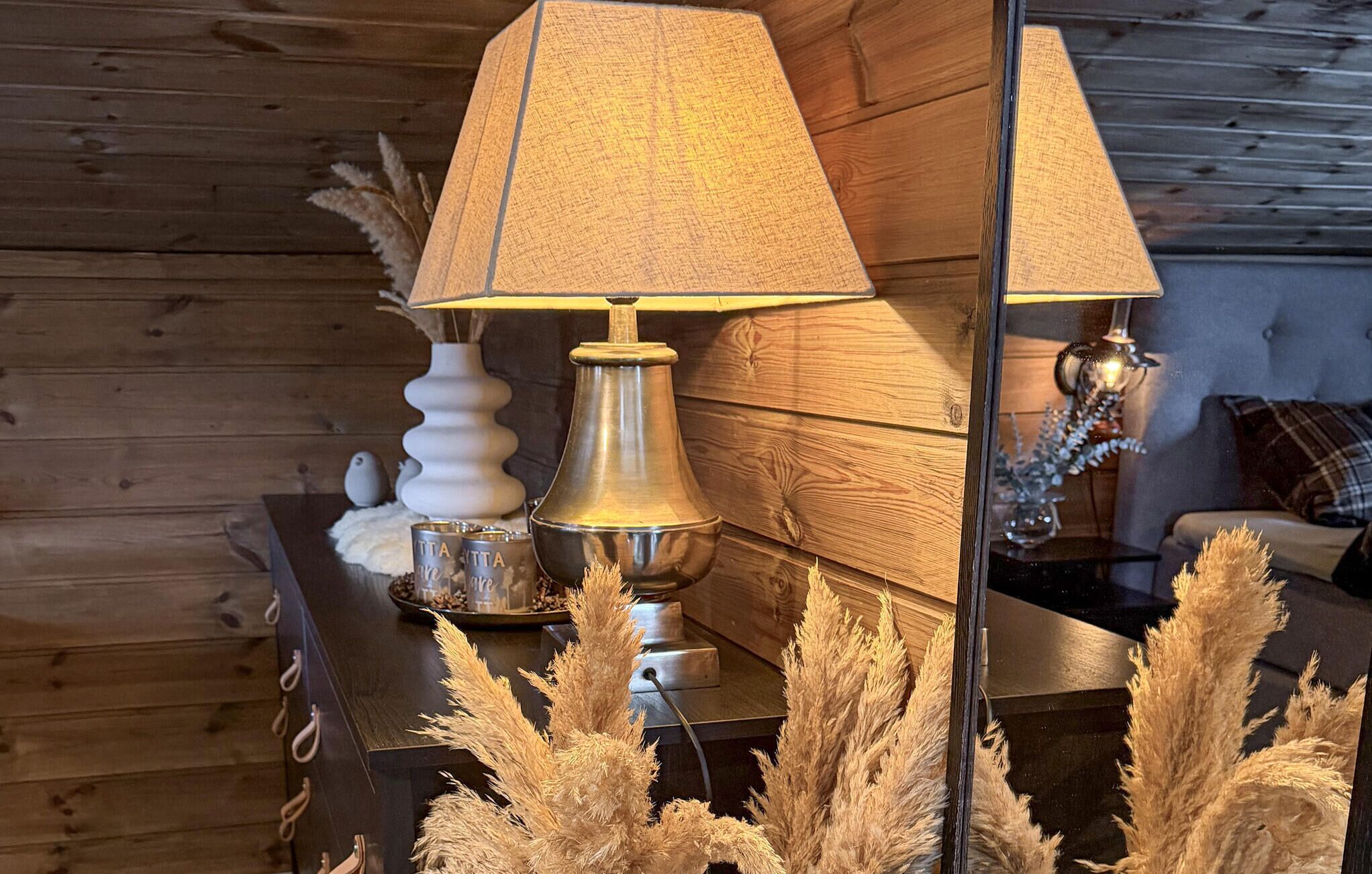 Ein Holzinterieur mit einer Lampe, einer Dekorationsvase und Pampasgras.