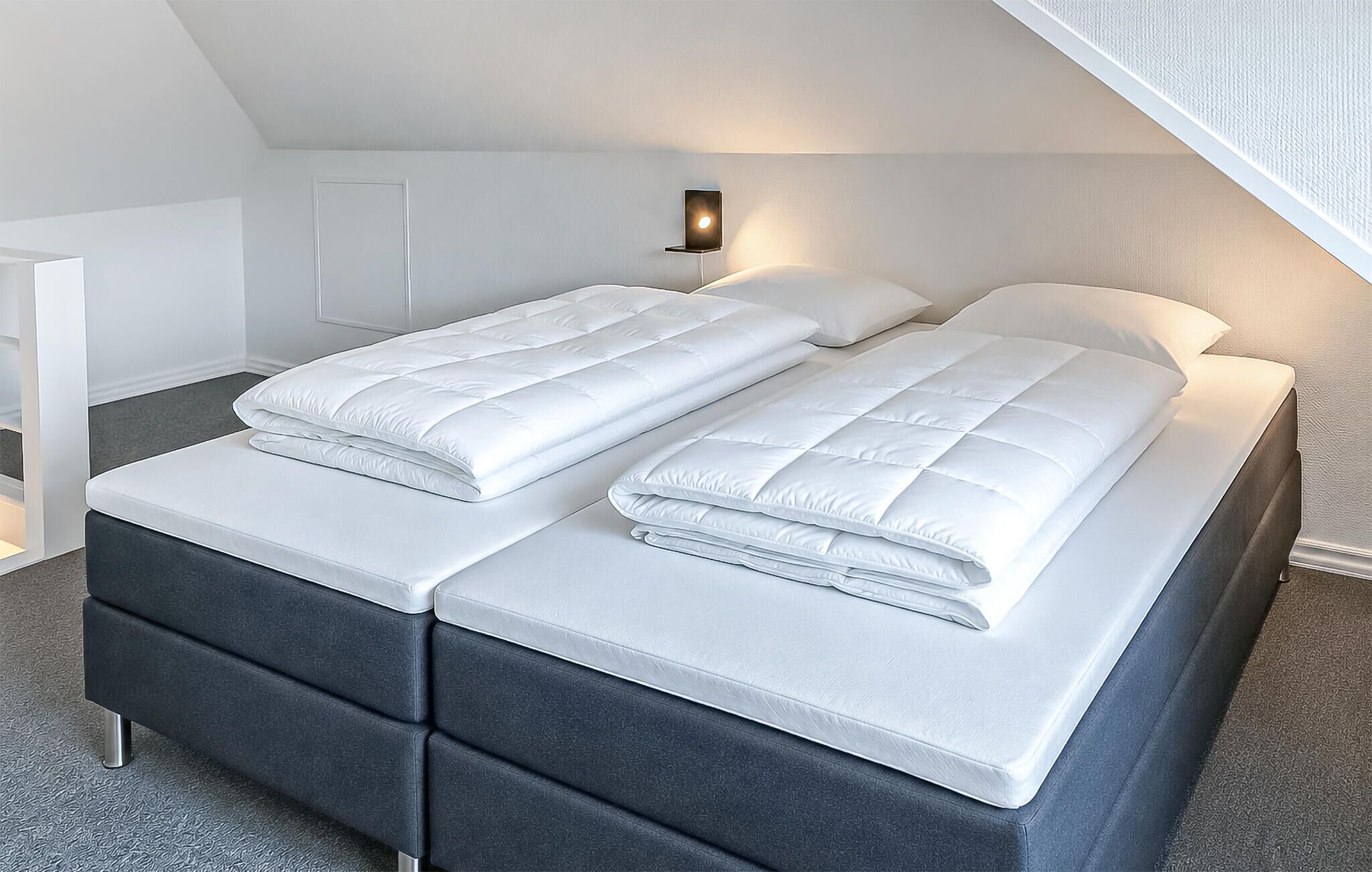 A neatly made twin bed with white bedding in a room with a sloped ceiling.