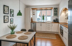 A compact kitchen with a dining area, wooden cabinets, a built-in oven, and a window with a view. - 3 bedroom amazing home in Hvide Sande (Hvide Sande)