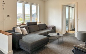 A modern living room with a grey sectional sofa, a small round coffee table, and a grey armchair. - 3 bedroom amazing home in Hvide Sande (Hvide Sande)