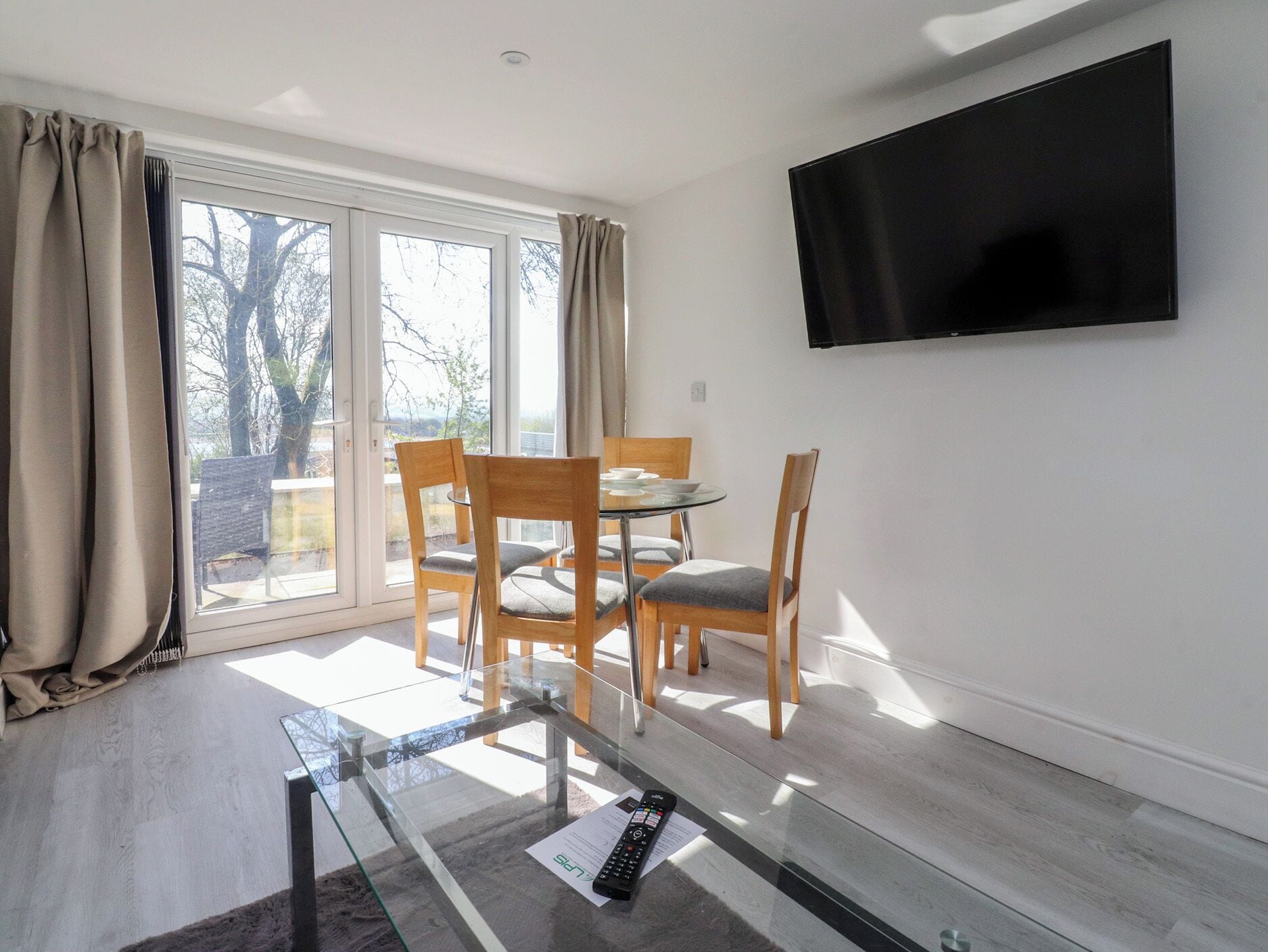 A room with a glass table, wooden chairs, a flat-screen TV, and a sliding glass door leading to an outdoor area.