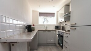 A compact kitchen with white cabinetry, a built-in oven, a microwave, and a kettle on the counter. - Beacon Fell Cottage 2 (Preston)