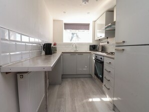 A compact kitchen with white cabinetry, a built-in oven, a microwave, and a kettle on the counter. - Beacon Fell Cottage 2 (Preston)