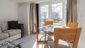 A modern living room with a glass dining table, wooden chairs, a sofa, and a view through large windows. - Beacon Fell Cottage 2 (Preston)