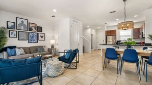 A modern living room with a sofa, ottoman, and dining area with chairs. - Walt's Disney Villa | Hot Tub & NO Resort Fees (Kissimmee)
