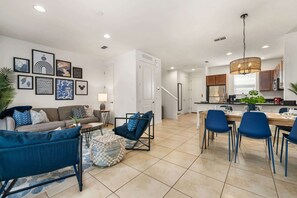 Un salon moderne avec un canapé, un pouf et un coin repas avec des chaises.
