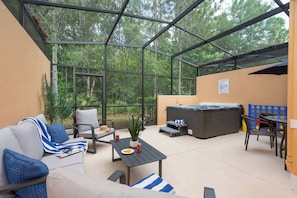 Eine überdachte Terrasse mit einer Couch, Stühlen, einem Tisch, einem Whirlpool und Blick auf den Wald.
