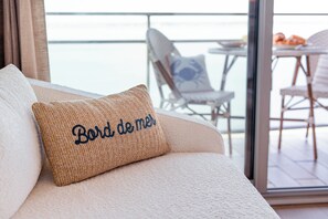 Ein Sofa mit einem gewebten Kissen und Blick auf einen Balkon mit Gartenmöbeln.