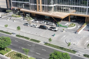 Ein modernes Hotel mit Glasfassade, einer angelegten Eingangspartie und einem Parkplatz mit mehreren Autos.