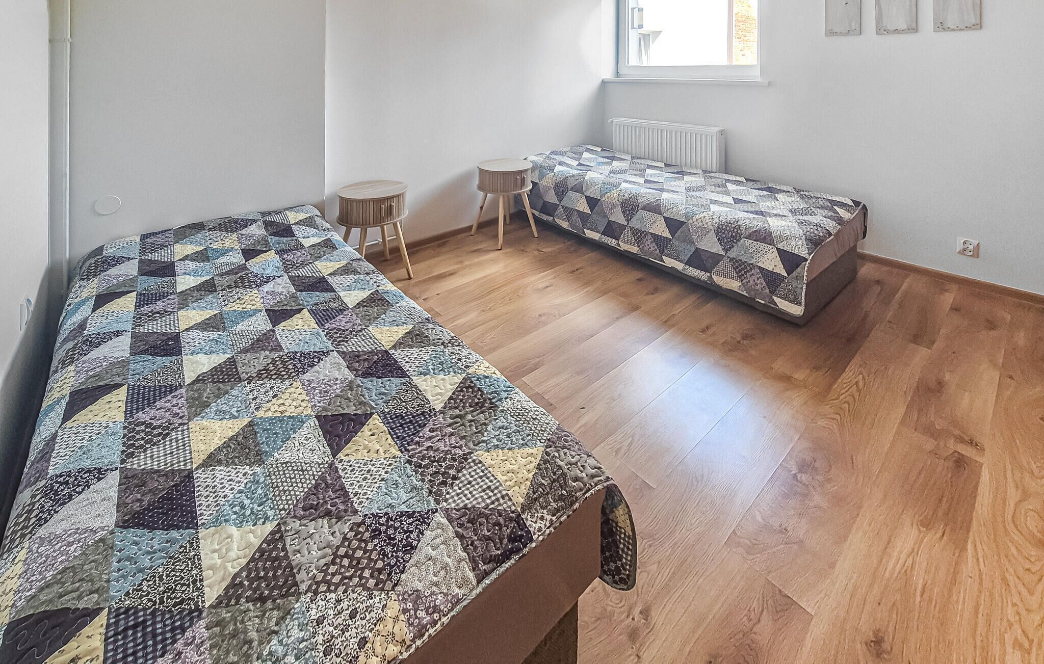 A room with two beds, a window, a radiator, and a small stool.