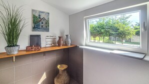 A bathroom with a window, a potted plant, a painting, and a shelf with decorative items. - Amazing apartment in Nowe Warpno with WiFi (Nowe Warpno)