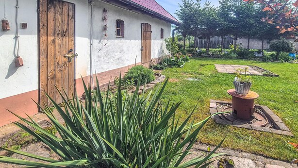 A building with a red roof, white walls, and wooden doors. There is a garden with grass, plants, and a small tree. - Amazing apartment in Nowe Warpno with WiFi (Nowe Warpno)