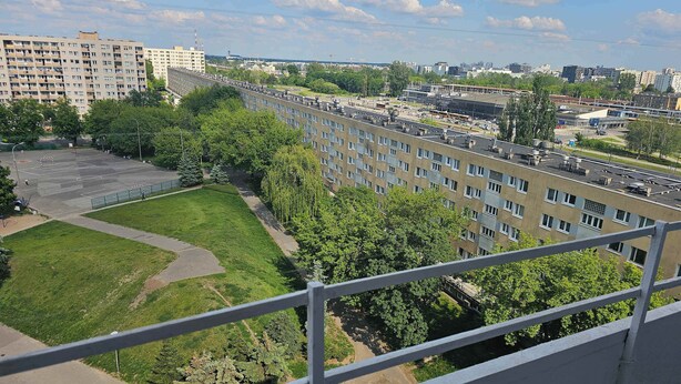 Un immeuble de grande hauteur, doté de nombreux étages, un patio avec pelouse et une vue sur les environs urbains.