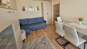 Un salon comprenant un canapé, une table à manger avec des chaises, un petit tapis et un vase avec des fleurs.