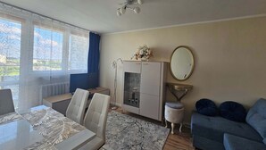 Une pièce comprenant une table à manger, des chaises, un canapé, un meuble avec un miroir et une fenêtre avec des rideaux.