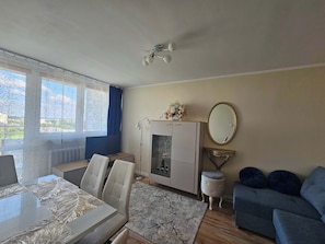 Una habitación con una mesa de comedor, sillas, un sofá, un armario con espejo y una ventana con cortinas.