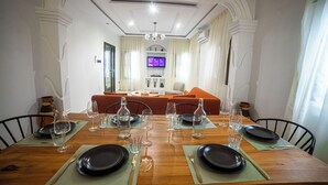 A dining area with a wooden table set for four, chairs, and a television in the background. - Villa Rosette, Calme, confort, services premiums (Lomé)