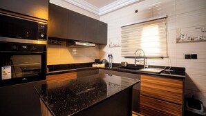 A modern kitchen with a black countertop, stainless steel appliances, wooden cabinets, and a window with blinds. - Villa Rosette, Calme, confort, services premiums (Lomé)