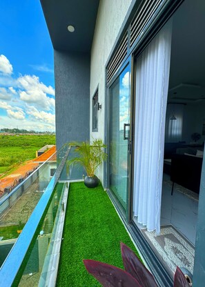 Ein Balkon mit Glastrennwand, einem Blumentopf und Blick auf eine grüne Landschaft.