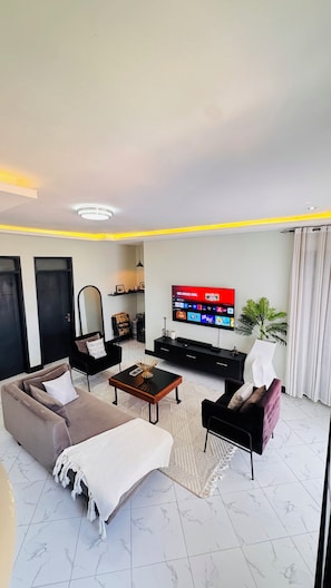 Ein Wohnzimmer mit Sofa, Sessel, Couchtisch, Fernseher und einer Pflanze.