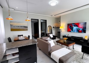 Ein modernes Wohnzimmer mit einer Couch, einem Esstisch, einem Fernseher und einem Bild mit einer Strandansicht.