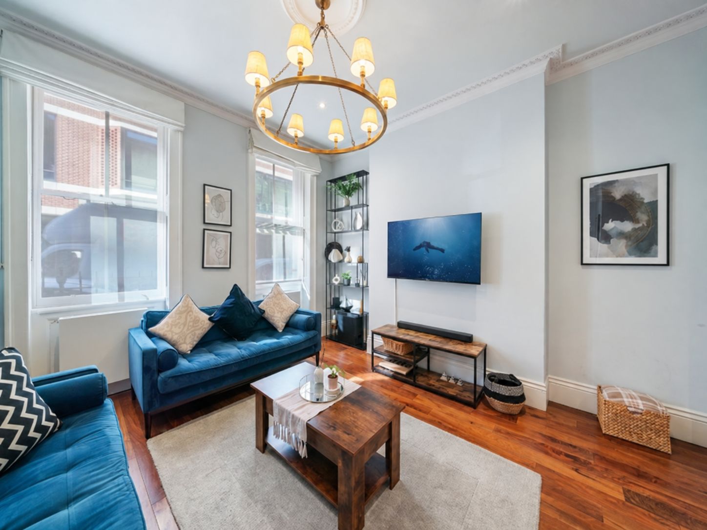 Ein Wohnzimmer mit einem blauen Sofa, einem Holztisch, einem Fernseher an der Wand und einer Kristallleuchter.