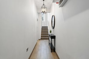 Ein Flur mit Treppe, einem schwarzen Beistelltisch mit Pflanze und einem Wandspiegel.
