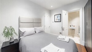 Ein modernes Schlafzimmer mit einem großen Bett, einem Nachttisch, einer Topfpflanze und einem Badezimmer mit Duschkabine.