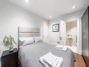 Ein modernes Schlafzimmer mit einem großen Bett, einem Nachttisch, einer Topfpflanze und einem Badezimmer mit Duschkabine.