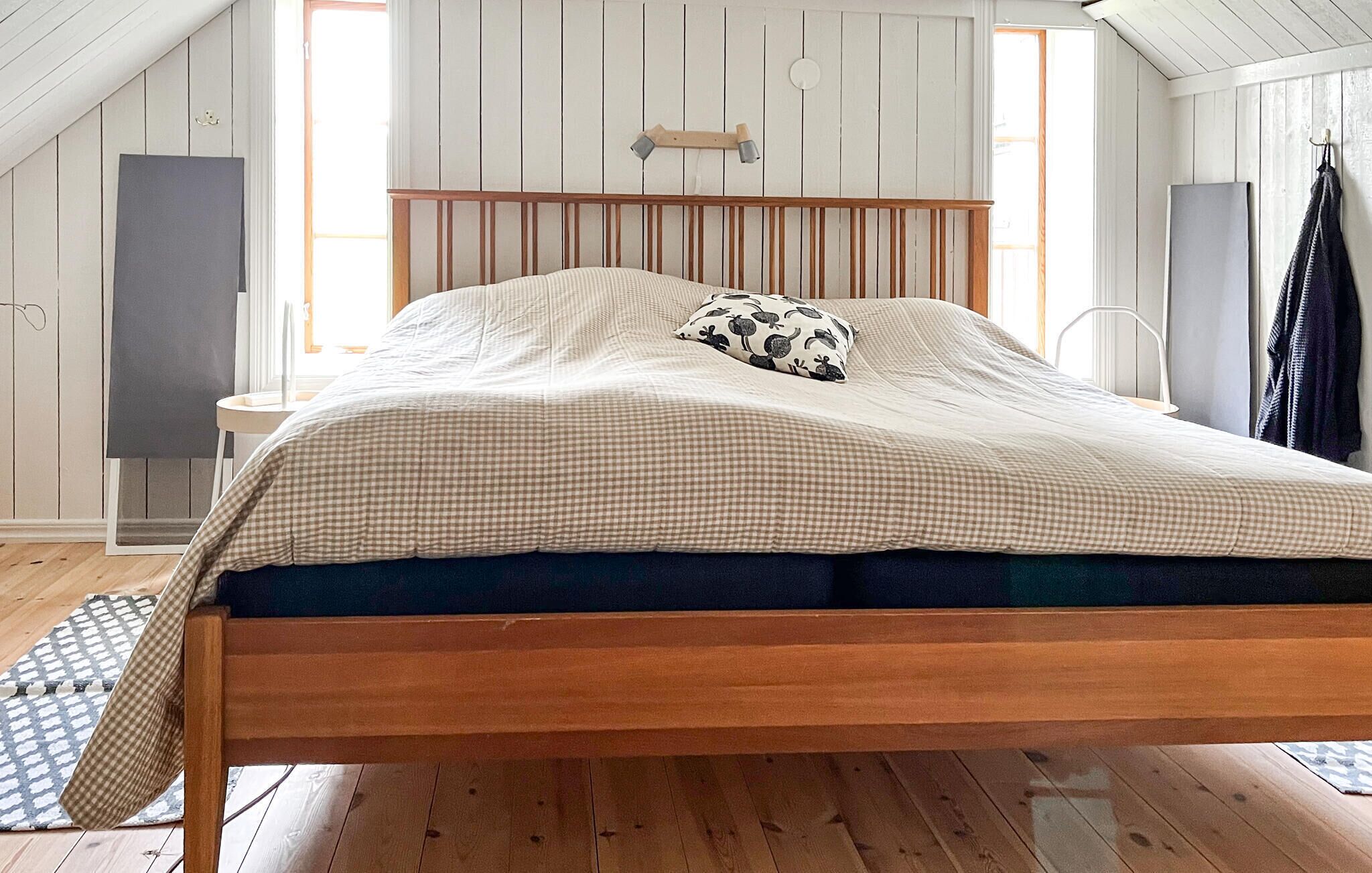 A bed with a wooden frame, a checkered bedspread, and a patterned pillow in a room with wooden walls and a sloped ceiling.