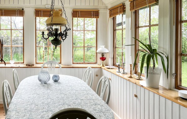 A dining room with a long table, chairs, a chandelier, and large windows with views of greenery. - Nice home in Fjälkinge (Fjälkinge)