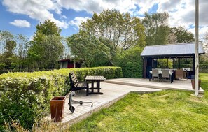 A wooden deck with a table and chairs, surrounded by well-maintained hedges and trees. - Nice home in Fjälkinge (Fjälkinge)