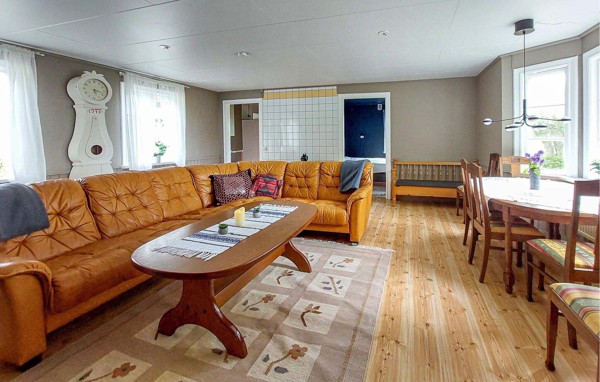 Ein Wohnzimmer mit einer Couch, einem Couchtisch, einem Esstisch mit Stühlen, einer Uhr und einem Fenster.