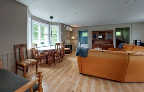 Ein geräumiges Wohnzimmer mit Holzboden, einer Couch, einem Esstisch mit Stühlen und einer Küchenzeile mit Schränken.