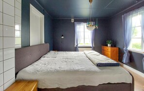 Ein Schlafzimmer mit Bett, Nachttisch, Kommode, Fenster und Deckenleuchte.