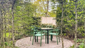 Ein runder Sitzbereich im Freien mit Tisch und Stühlen, umgeben von Bäumen und einem Steinweg.
