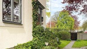 Ein Haus mit einem gepflasterten Weg, der zu einem Tor führt, umgeben von üppiger Vegetation und Bäumen.
