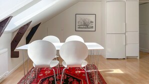 Ein zeitgemäßer Essbereich mit einem weißen Tisch und Stühlen, einem roten Teppich mit Muster und einem gerahmten Bild an der Wand.