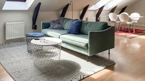 Ein modernes Schlafzimmer im Loft-Stil mit Dachfenster, einem grünen Sofa, einem runden Couchtisch und einem gemusterten Teppich.