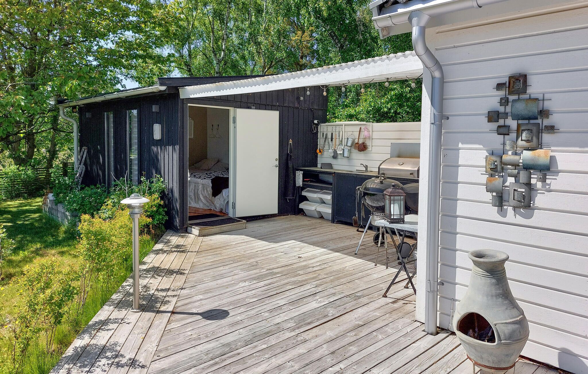 Eine Holzterrasse führt zu einer kleinen Hütte mit Küchenbereich, Schlafbereich und Grill.