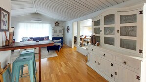 Ett rymligt vardagsrum med trägolv, ett matbord, blå stolar, en soffa och ett skåp med glasdörrar.